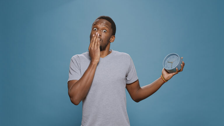 Shocked punctual man checking time on clock and running late